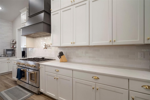 kitchen featuring tasteful backsplash, premium range hood, white cabinetry, and range with two ovens