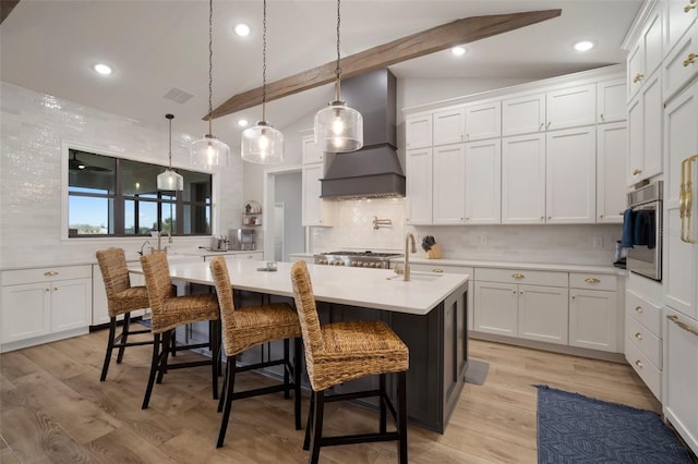 kitchen featuring lofted ceiling with beams, light wood-style flooring, oven, premium range hood, and a sink