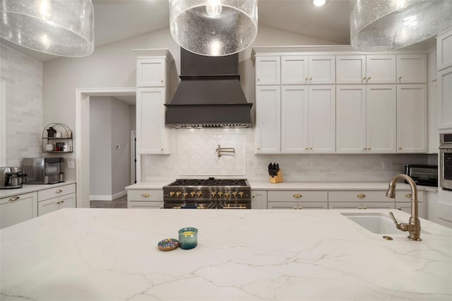 kitchen featuring stainless steel appliances, a sink, vaulted ceiling, backsplash, and custom range hood