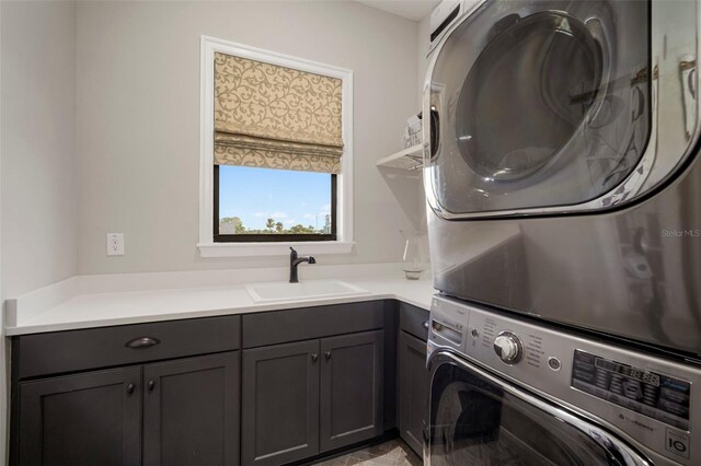 laundry area with stacked washer / drying machine, cabinet space, and a sink