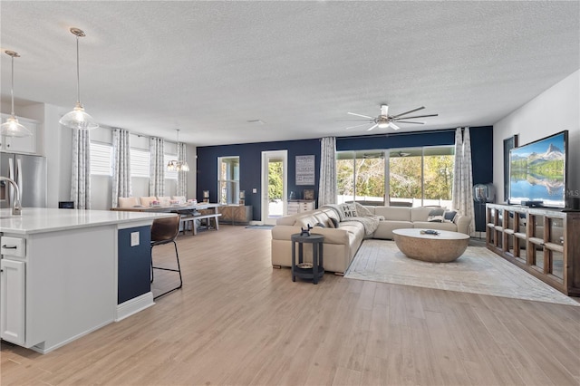 living room featuring light wood-type flooring, a ceiling fan, and a textured ceiling