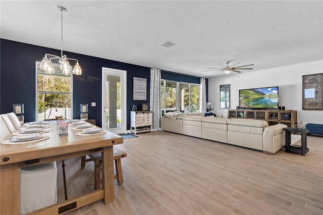 dining area featuring light wood-style floors, visible vents, a textured ceiling, and ceiling fan with notable chandelier