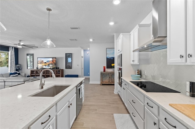 kitchen with visible vents, wall chimney exhaust hood, appliances with stainless steel finishes, open floor plan, and a sink