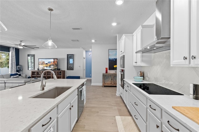 kitchen with wall chimney exhaust hood, appliances with stainless steel finishes, open floor plan, white cabinetry, and a sink