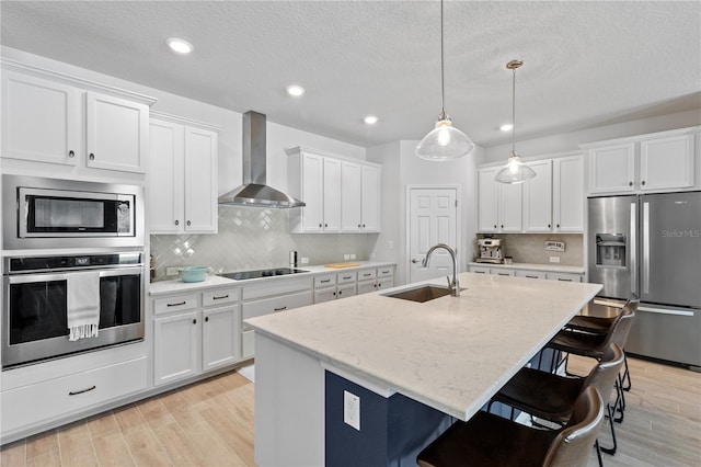 kitchen featuring stainless steel appliances, wall chimney range hood, a sink, and light wood-style flooring