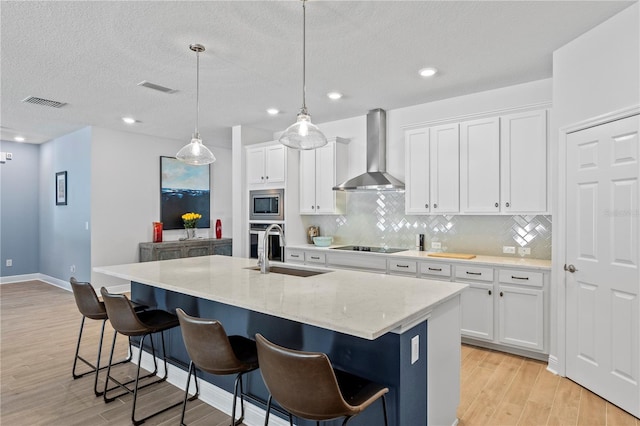 kitchen featuring visible vents, appliances with stainless steel finishes, light wood-style floors, a sink, and wall chimney exhaust hood