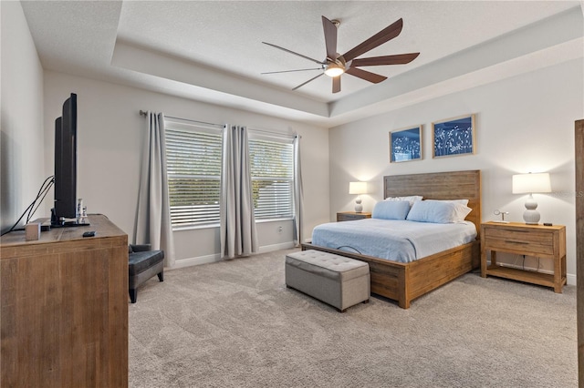 bedroom with a textured ceiling, light carpet, a ceiling fan, baseboards, and a raised ceiling