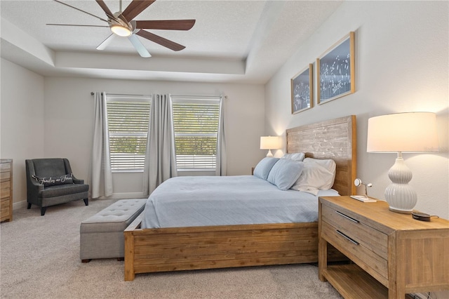 carpeted bedroom featuring a raised ceiling, ceiling fan, a textured ceiling, and baseboards