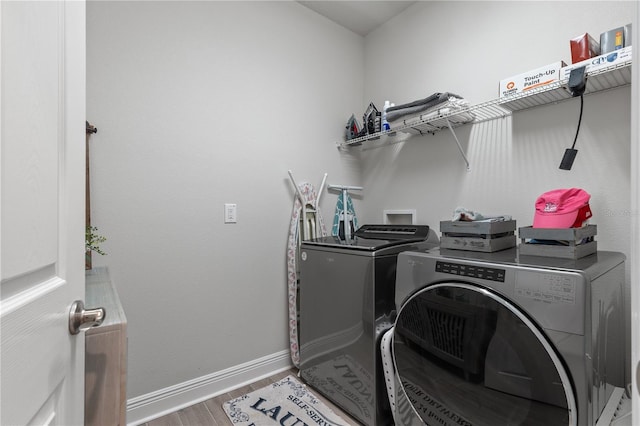 washroom featuring laundry area, separate washer and dryer, wood finished floors, and baseboards