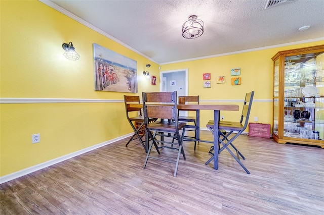 dining area featuring baseboards, a textured ceiling, ornamental molding, and wood finished floors