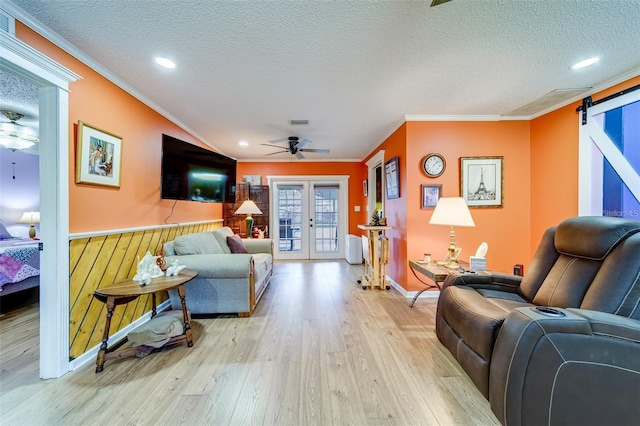 living area featuring a barn door, ornamental molding, light wood-style flooring, and french doors