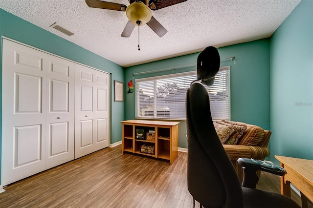 office space with a textured ceiling, wood finished floors, a ceiling fan, visible vents, and baseboards