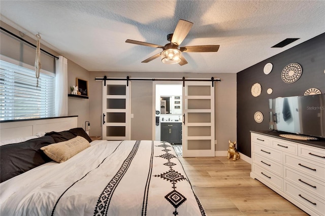 4118 Ramona Dr, Spring Hill, FL 34606 - bedroom featuring a barn door, light wood-style floors, a textured ceiling, ensuite bathroom, and a ceiling fan