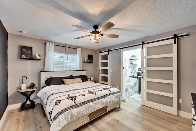 4118 Ramona Dr, Spring Hill, FL 34606 - bedroom featuring a barn door, light wood-type flooring, a textured ceiling, connected bathroom, and ceiling fan