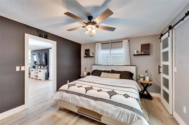 4118 Ramona Dr, Spring Hill, FL 34606 - bedroom with a barn door, light wood finished floors, a textured ceiling, and ceiling fan