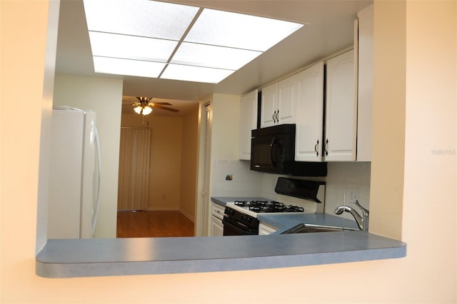 kitchen featuring a sink, range with gas stovetop, white cabinetry, freestanding refrigerator, and black microwave