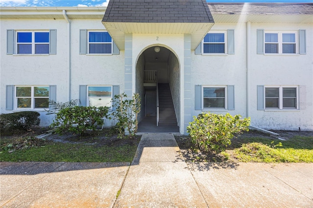 view of exterior entry featuring a shingled roof and stucco siding