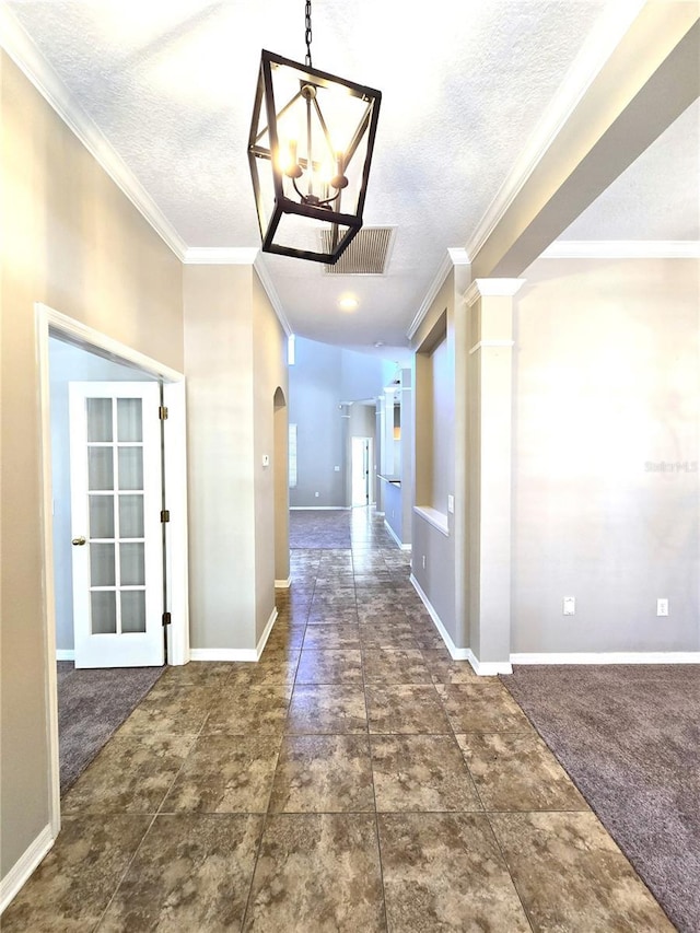 hallway featuring arched walkways, visible vents, an inviting chandelier, ornamental molding, and baseboards