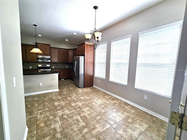 kitchen with baseboards, decorative backsplash, dark countertops, appliances with stainless steel finishes, and a notable chandelier