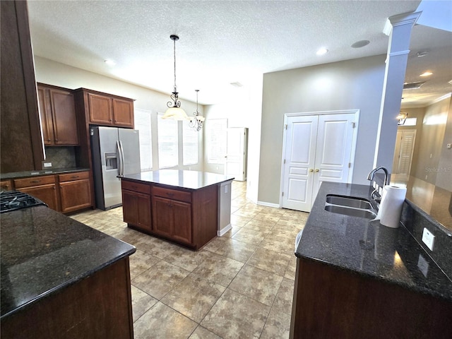 kitchen featuring a sink, a kitchen island, hanging light fixtures, stainless steel fridge with ice dispenser, and ornate columns