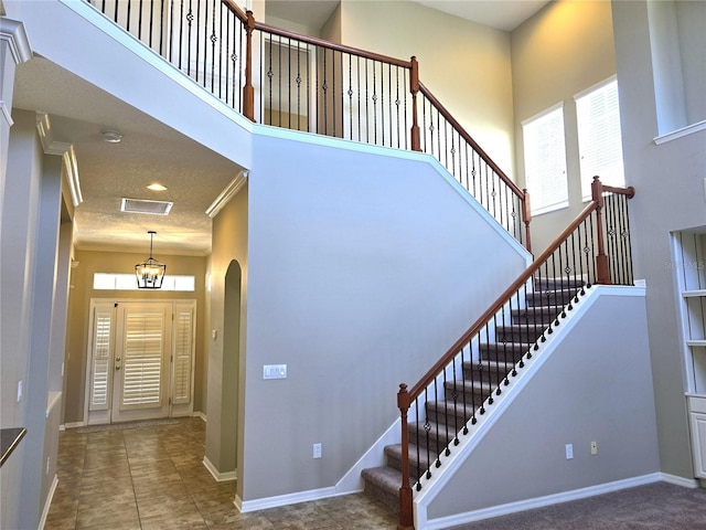 staircase with ornamental molding, a high ceiling, visible vents, and baseboards