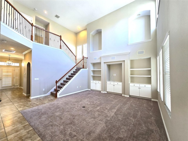 unfurnished living room with baseboards, visible vents, stairs, dark colored carpet, and built in shelves