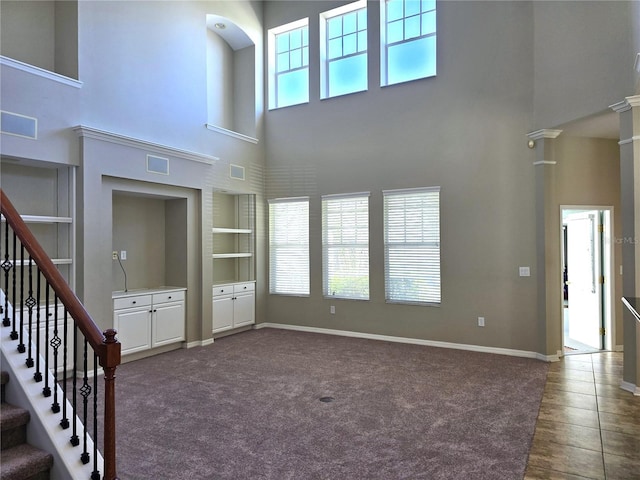 unfurnished living room with baseboards, stairs, built in features, dark carpet, and ornate columns