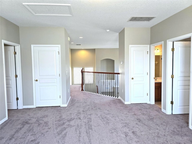 carpeted spare room with attic access, visible vents, a textured ceiling, and baseboards