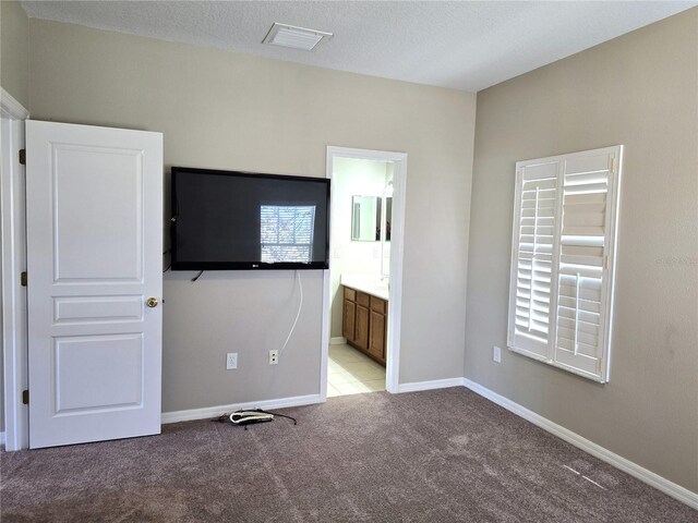 unfurnished bedroom featuring light colored carpet, visible vents, a textured ceiling, ensuite bath, and baseboards