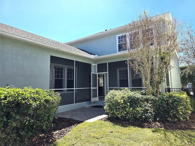 rear view of house featuring a sunroom, a shingled roof, a lawn, and stucco siding