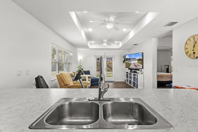 kitchen with a tray ceiling, recessed lighting, visible vents, open floor plan, and a sink