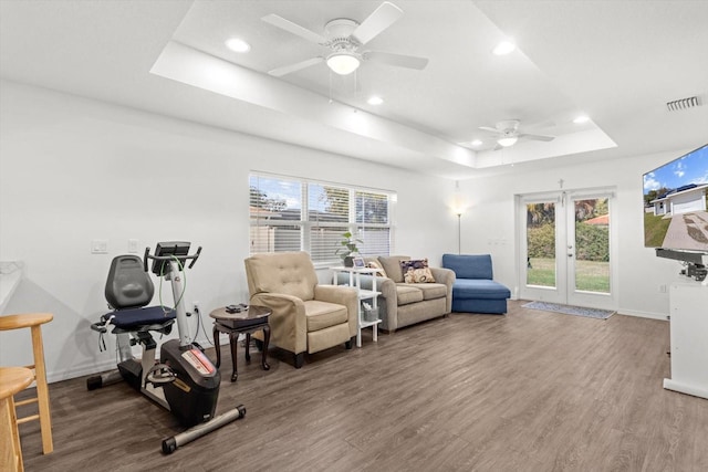 living area with a tray ceiling, wood finished floors, visible vents, and a ceiling fan