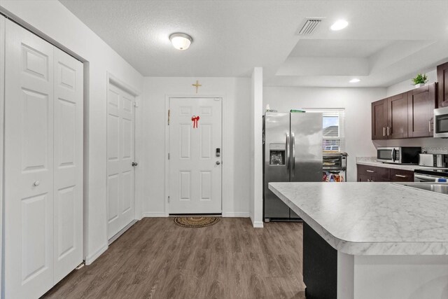 kitchen with stainless steel appliances, a raised ceiling, visible vents, dark brown cabinetry, and wood finished floors