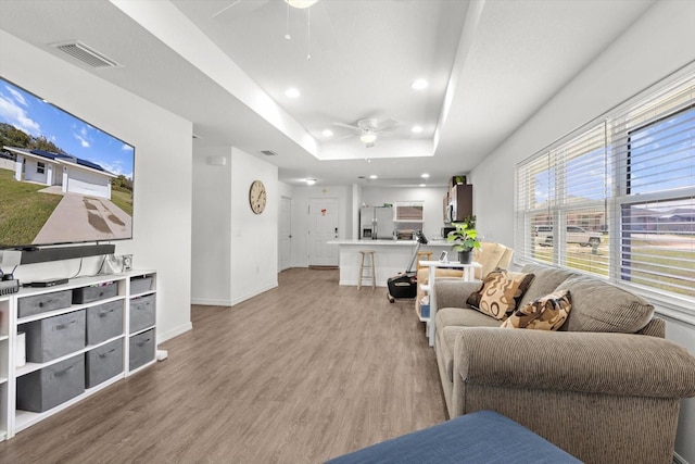 living room with ceiling fan, a tray ceiling, visible vents, and light wood-style floors