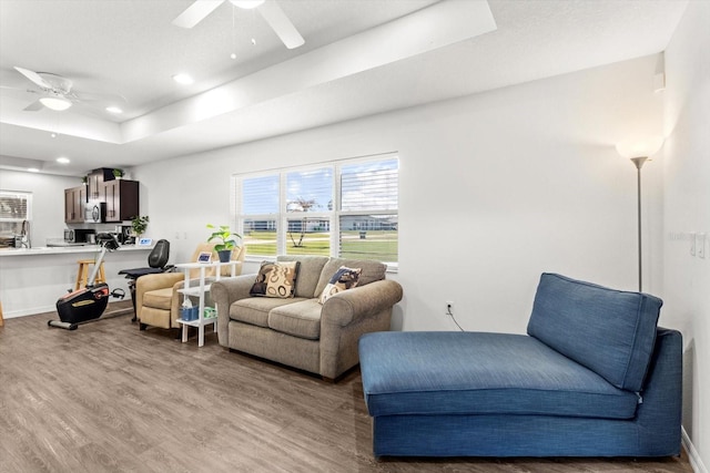 living area with light wood finished floors, a tray ceiling, and a ceiling fan