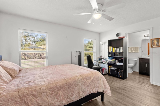 bedroom featuring baseboards, a ceiling fan, ensuite bath, wood finished floors, and a textured ceiling