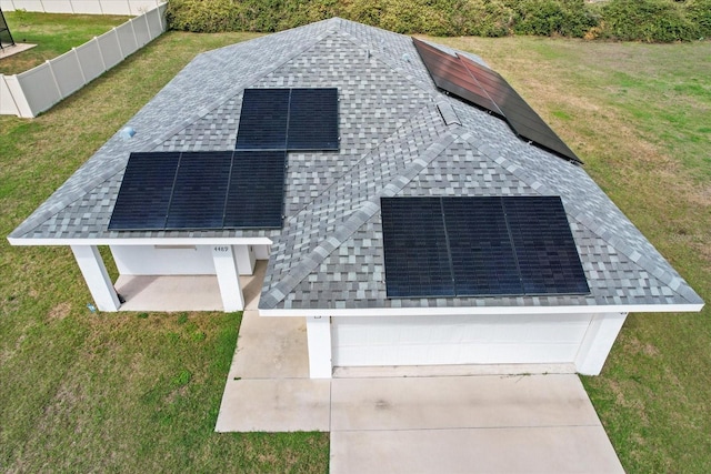 view of front of home featuring a shingled roof, fence, a front lawn, and solar panels