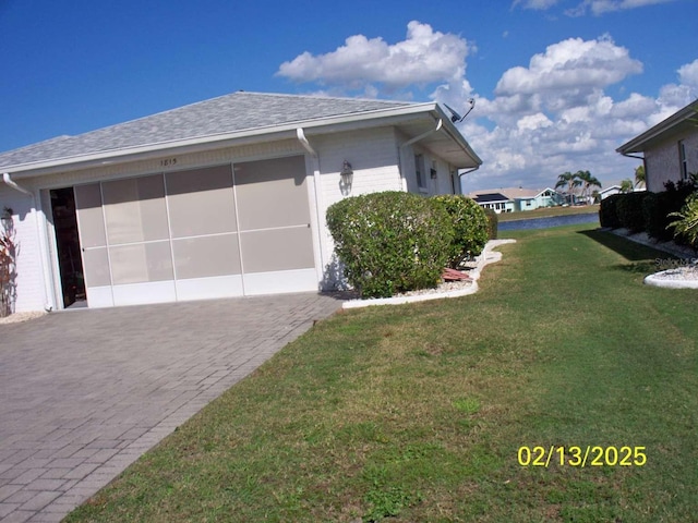 view of side of home featuring decorative driveway, brick siding, a yard, a shingled roof, and a garage