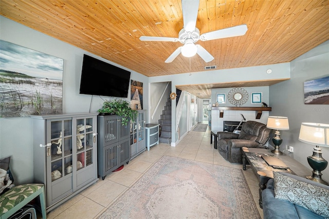 tiled living area with visible vents, wood ceiling, ceiling fan, a tile fireplace, and stairs