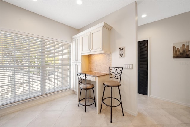 kitchen with a kitchen bar, light stone counters, light tile patterned floors, decorative backsplash, and baseboards