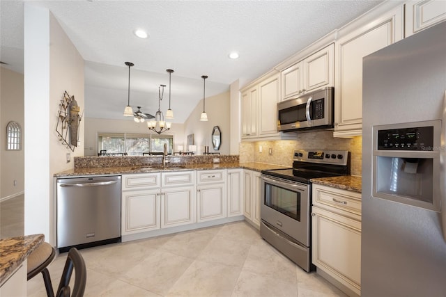 kitchen with cream cabinetry, a sink, dark stone countertops, appliances with stainless steel finishes, and decorative backsplash