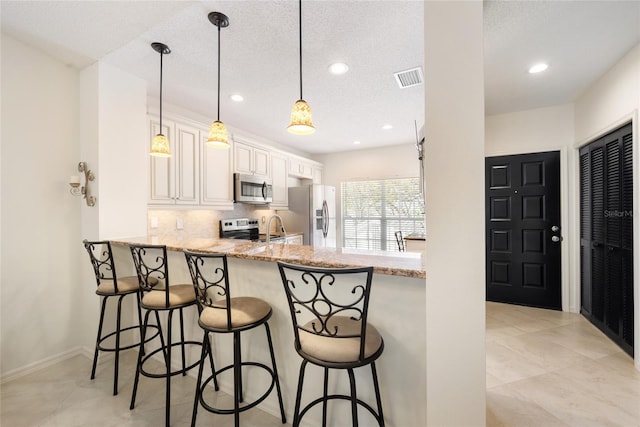 kitchen with visible vents, light stone counters, stainless steel appliances, a peninsula, and decorative backsplash