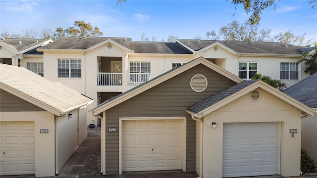 townhome / multi-family property with a garage, a balcony, a shingled roof, and stucco siding