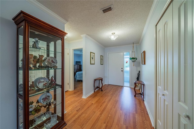 entrance foyer with visible vents, a textured ceiling, light wood-style floors, and ornamental molding