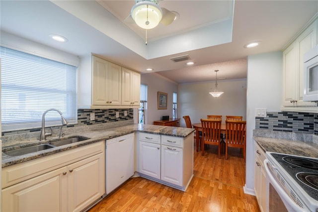 kitchen with white appliances, visible vents, a peninsula, a tray ceiling, and a sink