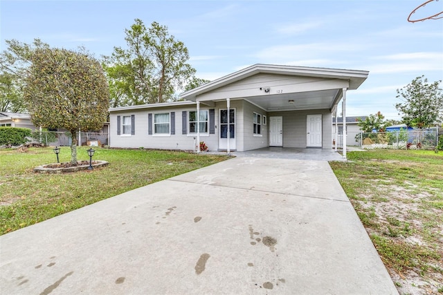 ranch-style house with concrete block siding, concrete driveway, a front yard, fence, and a carport