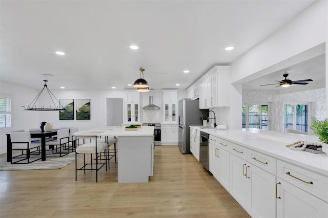 kitchen with light wood finished floors, wall chimney exhaust hood, appliances with stainless steel finishes, and a breakfast bar