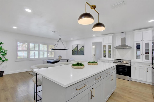 kitchen featuring a kitchen island, electric stove, wall chimney range hood, light countertops, and light wood finished floors