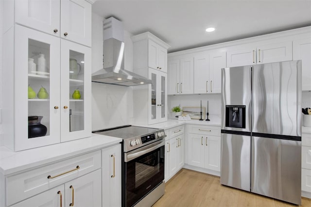 kitchen featuring light wood-style flooring, appliances with stainless steel finishes, glass insert cabinets, white cabinets, and wall chimney exhaust hood