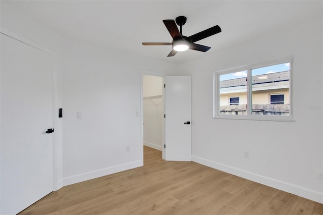 unfurnished bedroom with light wood-type flooring, a spacious closet, baseboards, and a ceiling fan